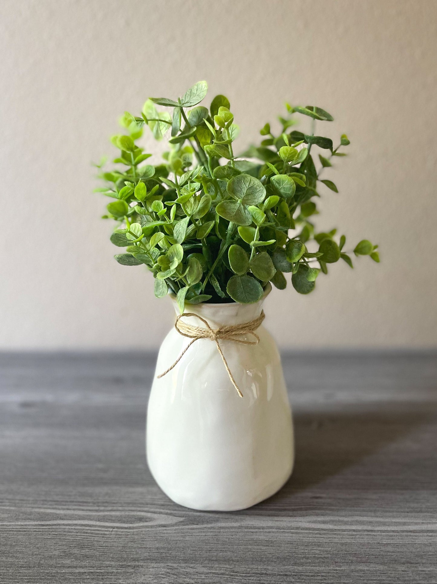 a small glossy creamy white ceramic vase with twine wrapped around the fluted top of the vase and eucalyptus coming out of the top of the vase. A perfect addition to a farmhouse style home.